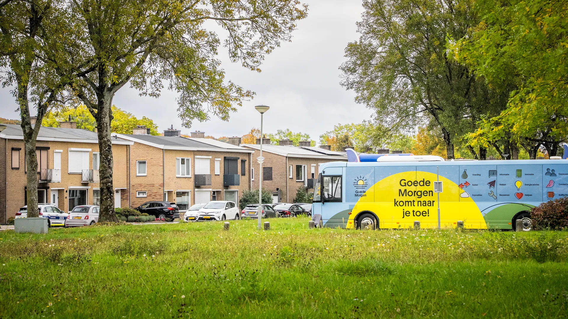 Bus met duurzame boodschap "Goede Morgen komt naar je toe" rijdt door woonwijk met rijtjeshuizen en bomen.